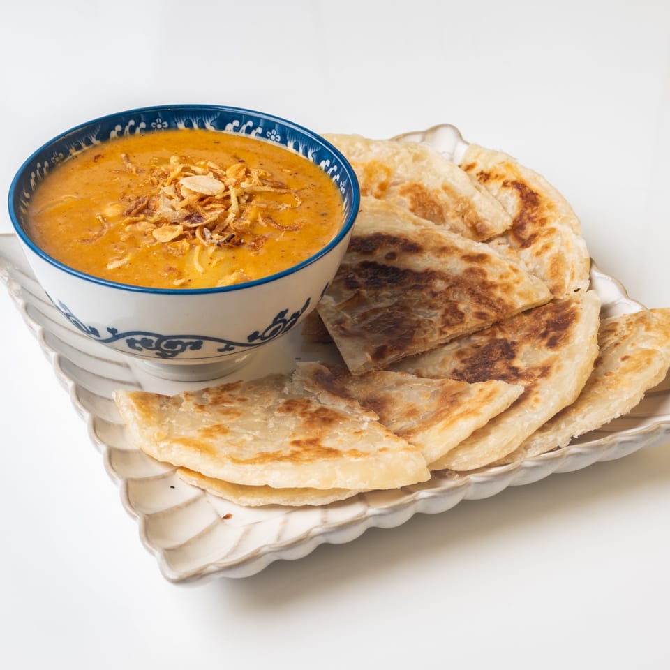 A blue and white bowl of yellow curry with crispy onions, next to a plate of roti.