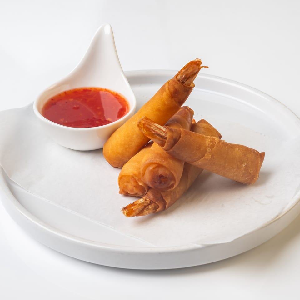 Crispy golden fried shrimp spring rolls with a side of sweet chili dipping sauce on a white plate.