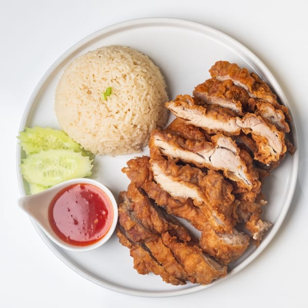 KorKai Thai Restaurant's fried chicken with rice, sliced cucumbers, and sweet chili sauce on a white plate.