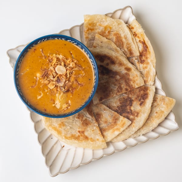 KorKai Thai Restaurant's yellow curry with crispy fried onions, served with flaky roti bread on a white plate.
