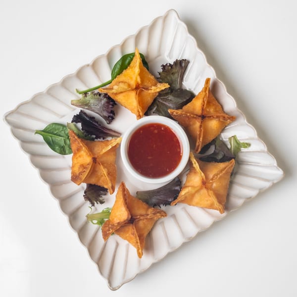 Crispy golden KorKai Thai crab rangoons arranged on a scalloped plate with a sweet chili dipping sauce.