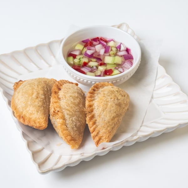 Three golden-brown KorKai Thai curry puffs with a side of sweet and sour dipping sauce.
